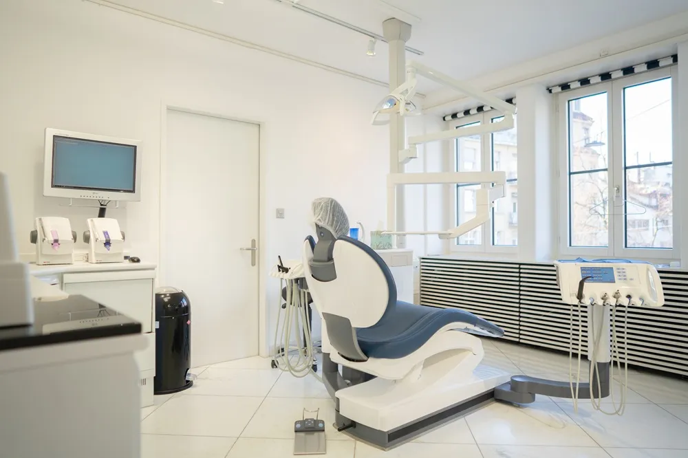 Behandlungszimmer der Praxis Zürich mit Behandlungsstuhl, Bildschirm und Fenstern zur Strasse