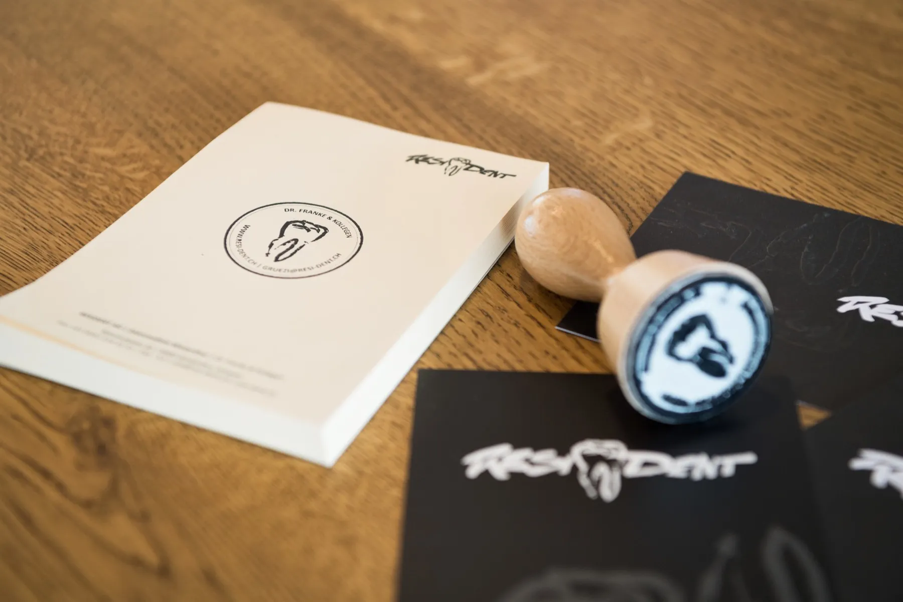 Praxisstempel, Notizblock und Karten mit dem Resident-Schriftzug auf einem Holztisch